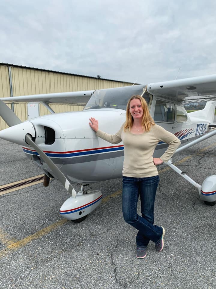 Woman Standing by Small White Plane Near Hanger with Hangarkeepers Insurance 